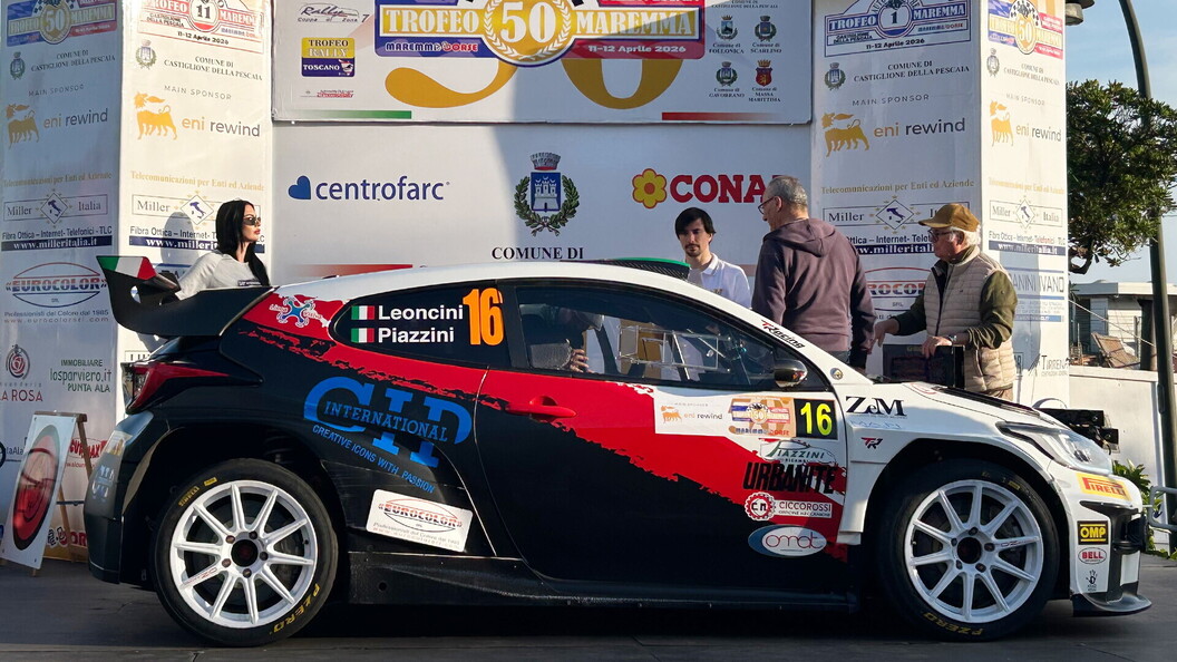 L'auto numero 16 di Leoncini e Piazzini, una Skoda con livrea nera, bianca e rossa e sponsor CT International, parcheggiata davanti a uno striscione del rally con diversi loghi. Quattro persone sono in piedi dietro l'auto.