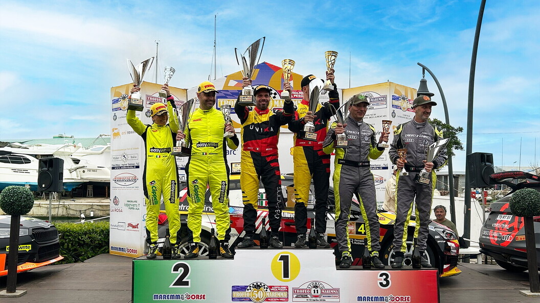 I sei piloti e copiloti saliti sul podio del 50° Trofeo Maremma sollevano i loro trofei, posando davanti a uno striscione con i nomi degli sponsor.