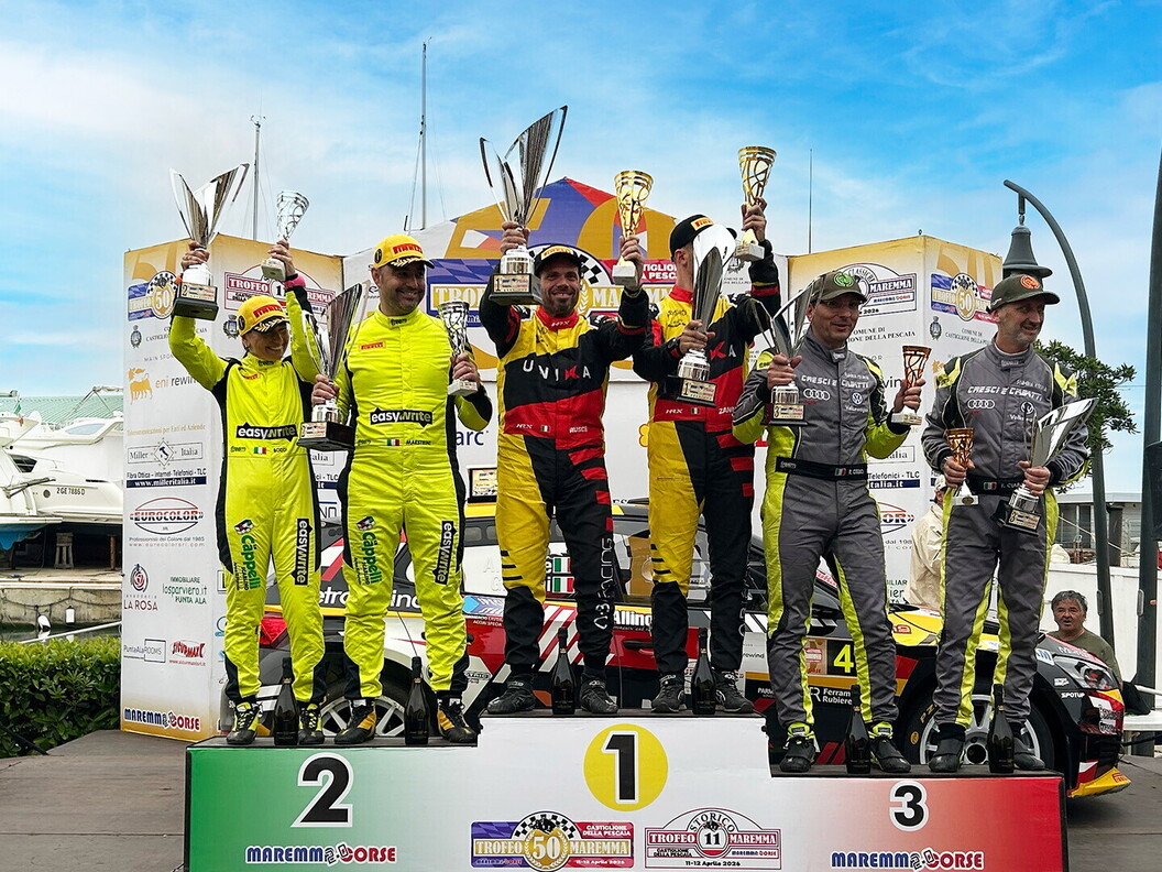 The top three winning teams of the rally standing on the podium, holding trophies.